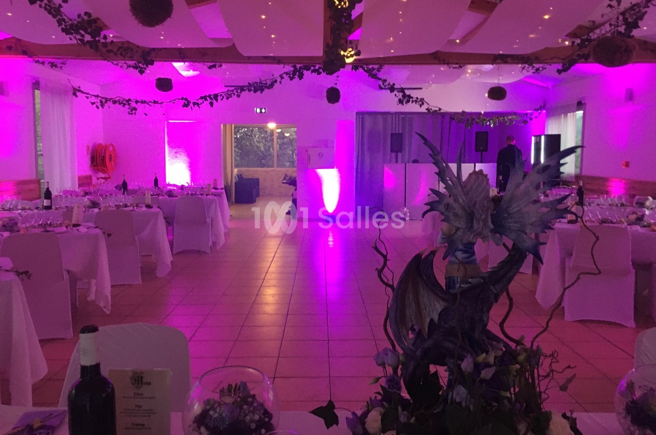 Salle de réception décorée pour un événement, éclairée par des lumières violettes et ornée de plantes et d'éléments festifs.