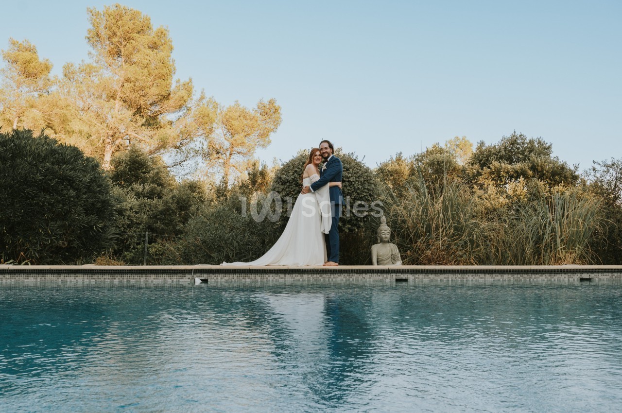 Un couple debout sur le bord d'une piscine, entouré de végétation et d'une statue de Bouddha.