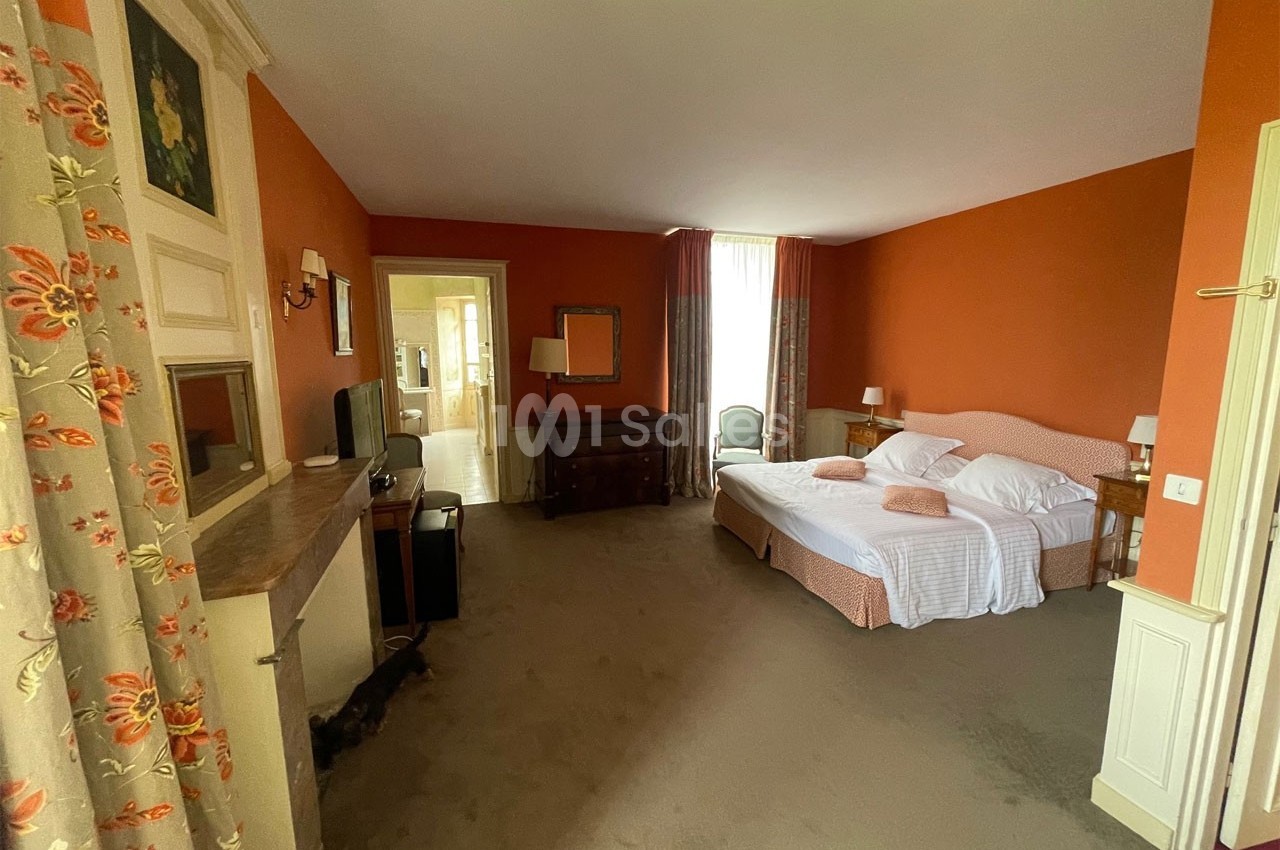 Chambre spacieuse avec murs orange, lit double, mobilier en bois, télévision et grande fenêtre avec rideaux.