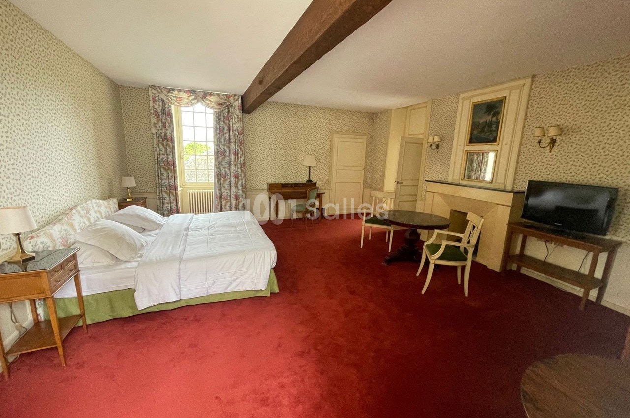 Chambre spacieuse avec lit double, moquette rouge, mobilier classique, télévision et grande fenêtre avec rideaux fleuris.