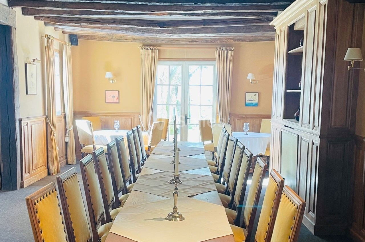 Salle à manger lumineuse avec une grande table en bois, chaises rembourrées et fenêtres donnant sur un jardin.