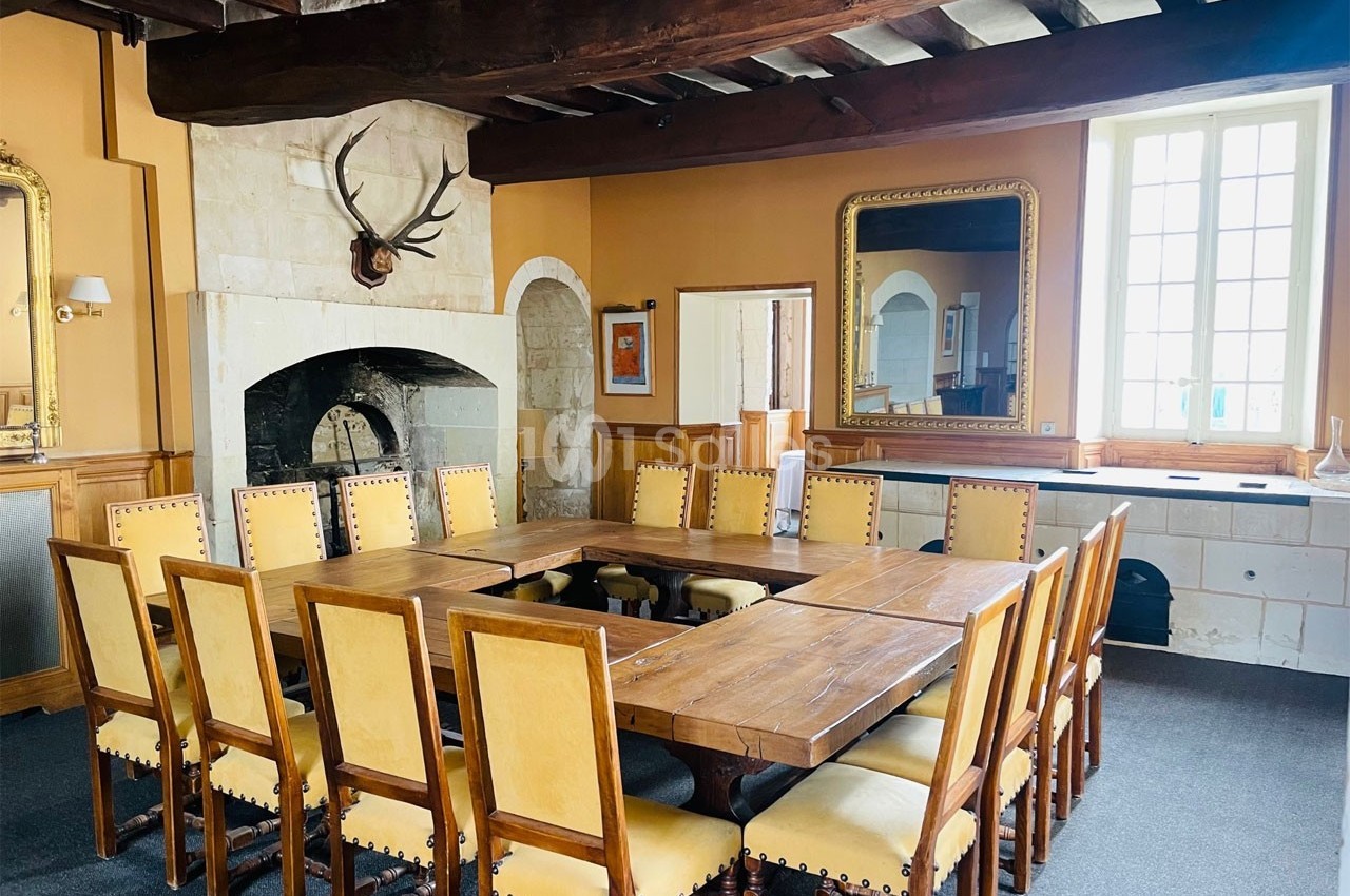 Salle à manger rustique avec grande table en bois, chaises cloutées, cheminée en pierre et miroirs muraux.