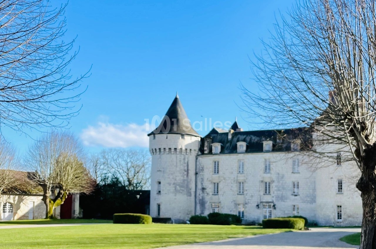 Château en pierre blanche avec tours et toit en ardoise, entouré d'arbres et d'une pelouse sous un ciel bleu.
