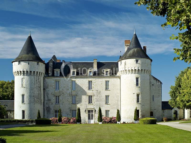 Château en pierre blanche avec deux tours rondes, entouré de pelouse et d'arbres sous un ciel dégagé.