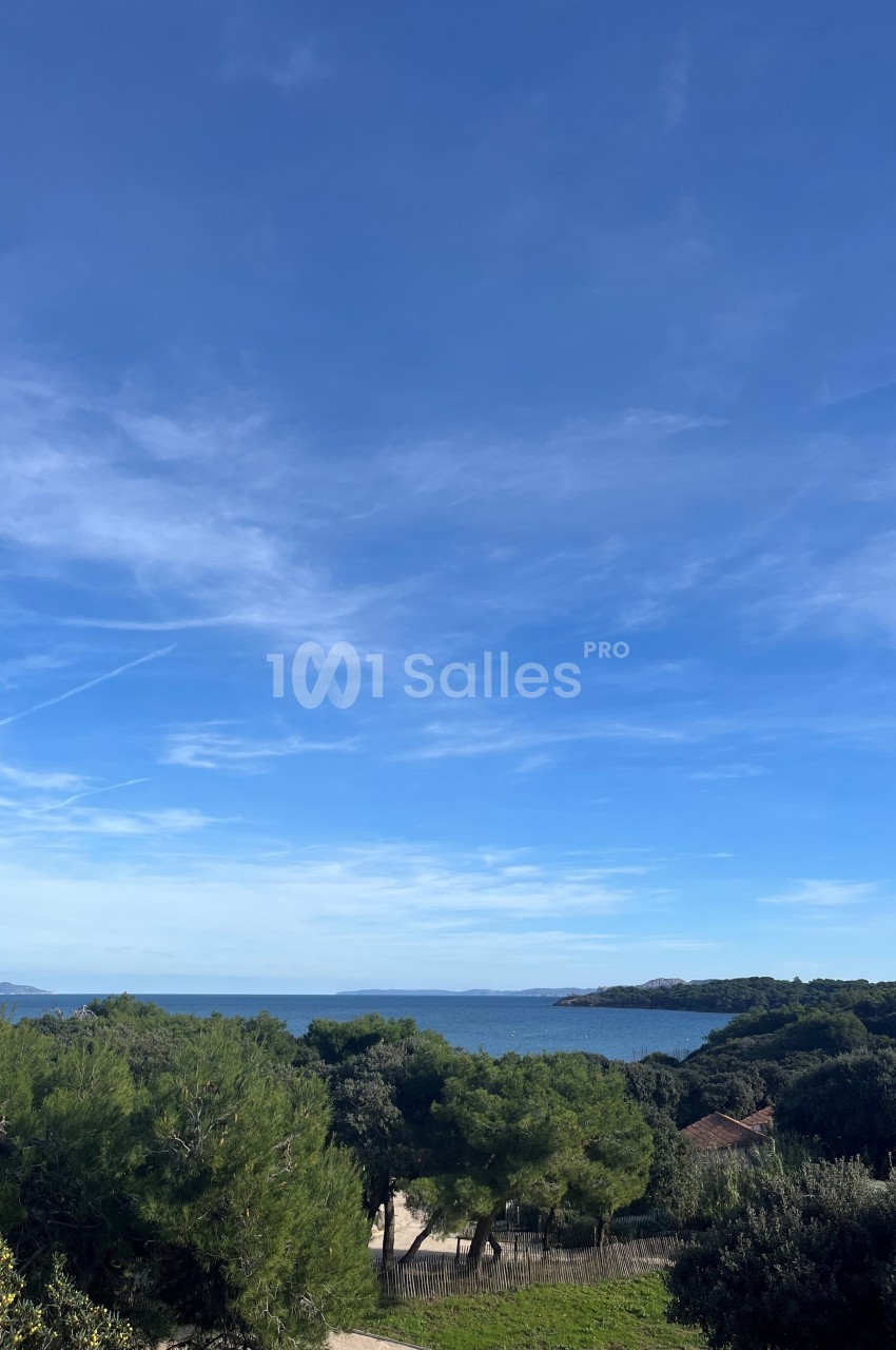Vue sur une côte méditerranéenne avec des arbres, une plage, la mer et un ciel bleu dégagé.