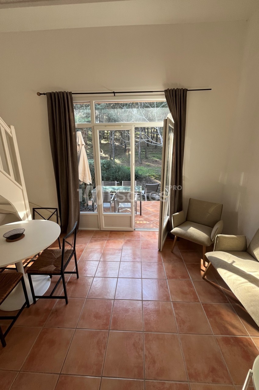 Vue d'un salon lumineux avec carrelage, table ronde, fauteuils, et porte-fenêtre ouverte sur une terrasse et un jardin.