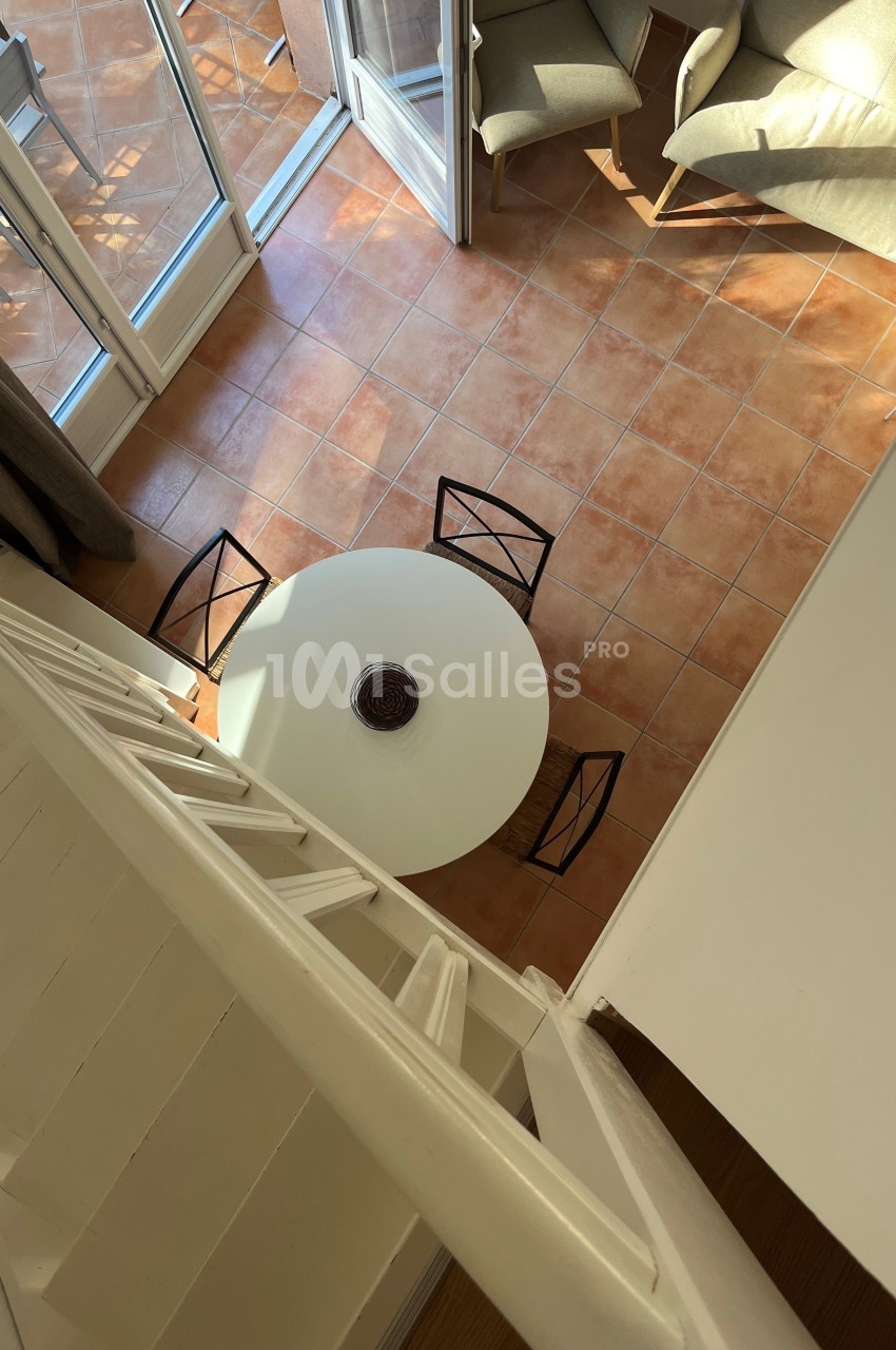 Vue plongeante sur une table ronde blanche entourée de chaises noires, dans un salon avec carrelage et mobilier clair.