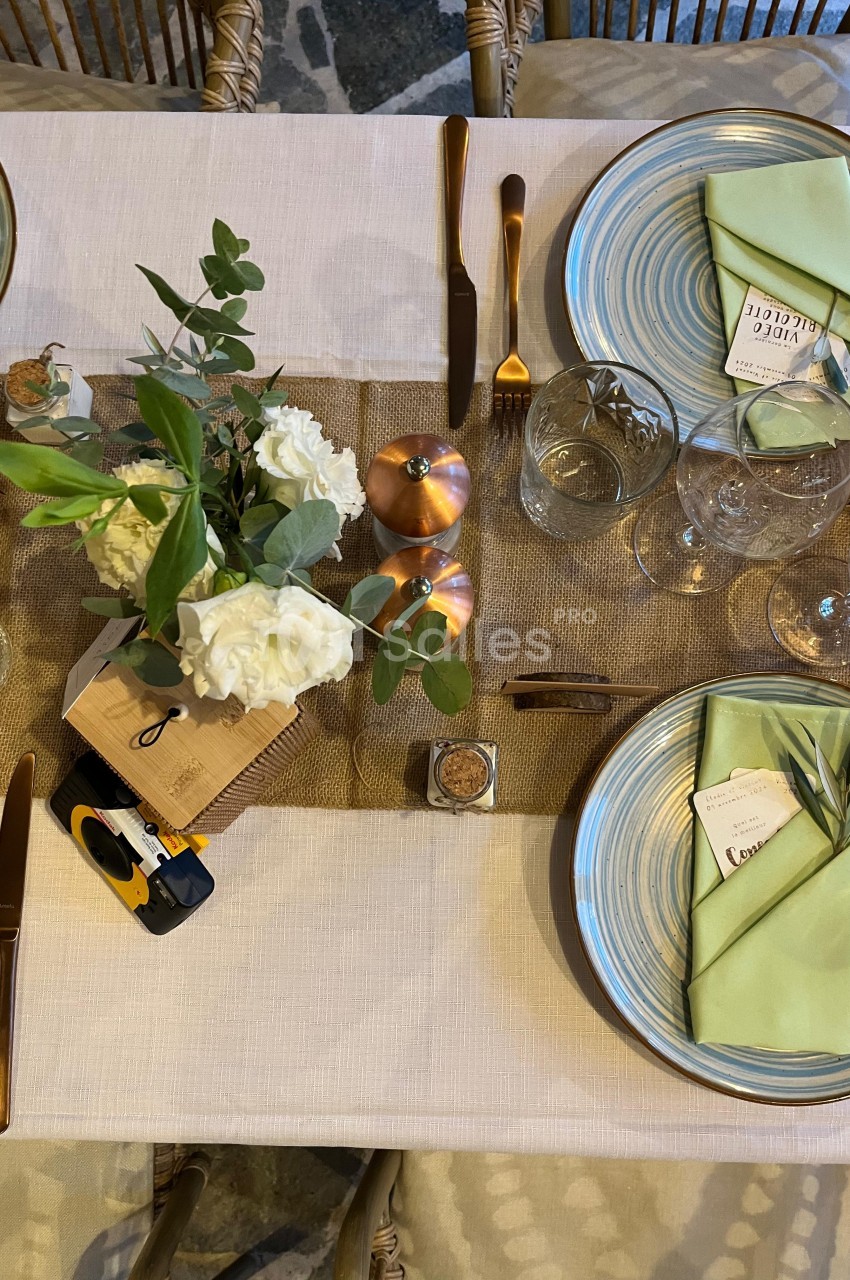 Table dressée avec vaisselle en céramique, serviettes vertes, couverts dorés, fleurs blanches et décoration en cuivre.