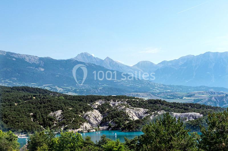 Paysage de montagne avec lac turquoise entouré de forêts et collines sous un ciel dégagé.