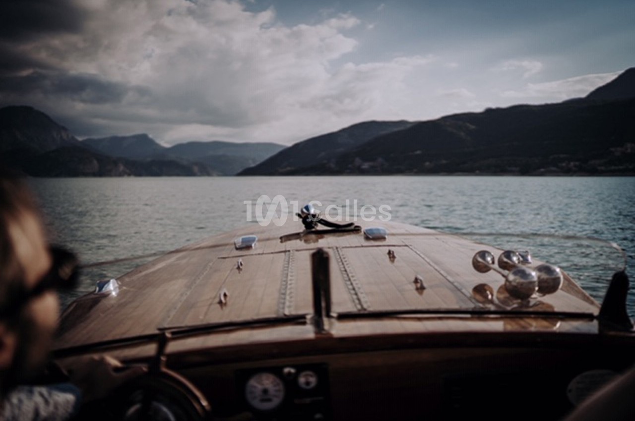 Vue depuis un bateau en bois naviguant sur un lac entouré de montagnes sous un ciel partiellement nuageux.