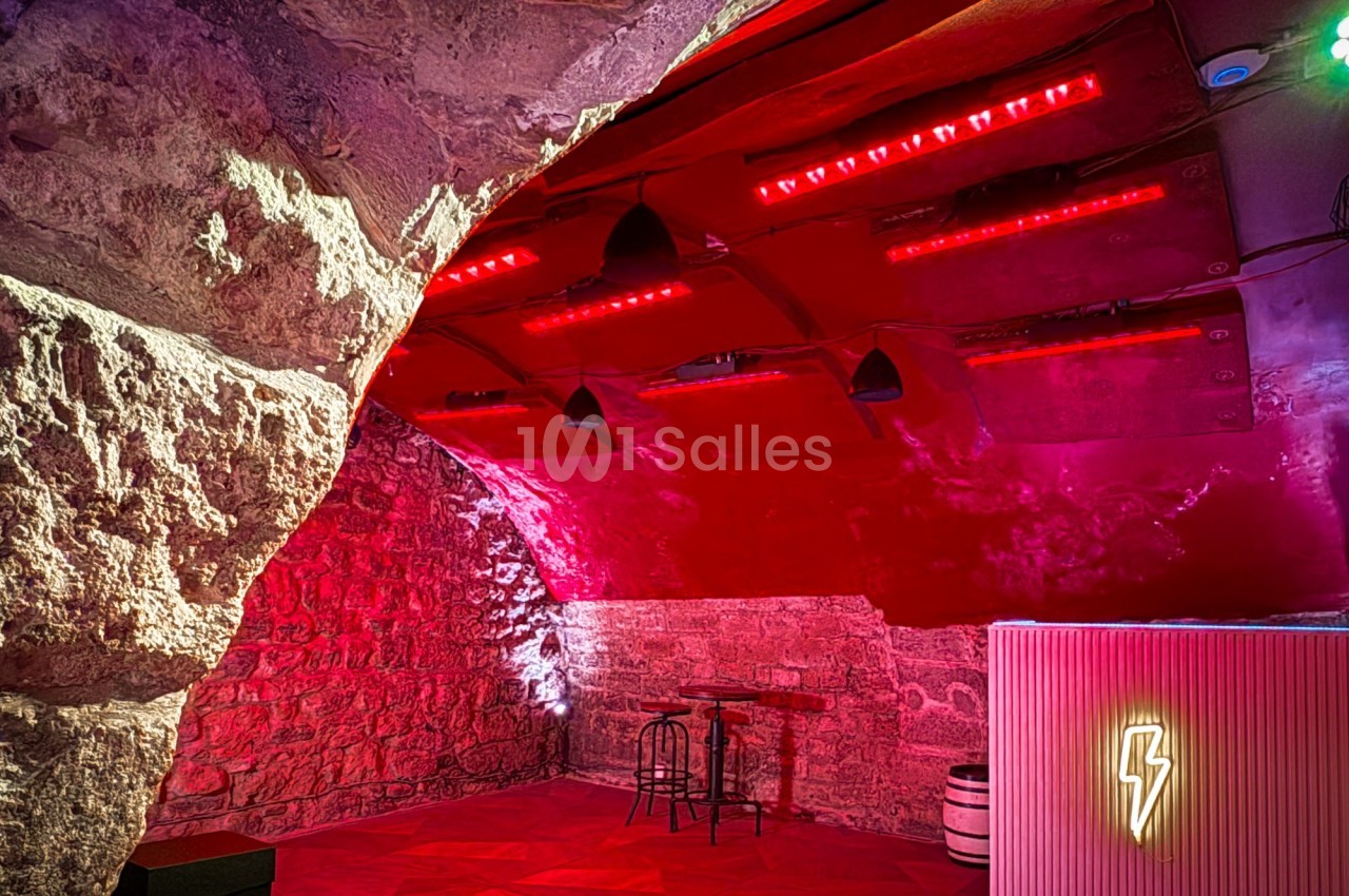 Salle voûtée en pierre avec éclairage rouge, un bar lumineux et quelques meubles minimalistes.
