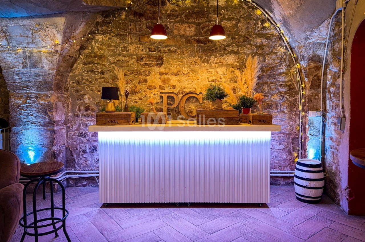 Comptoir lumineux dans une pièce voûtée en pierre, décoré de plantes, lampes et guirlandes lumineuses.