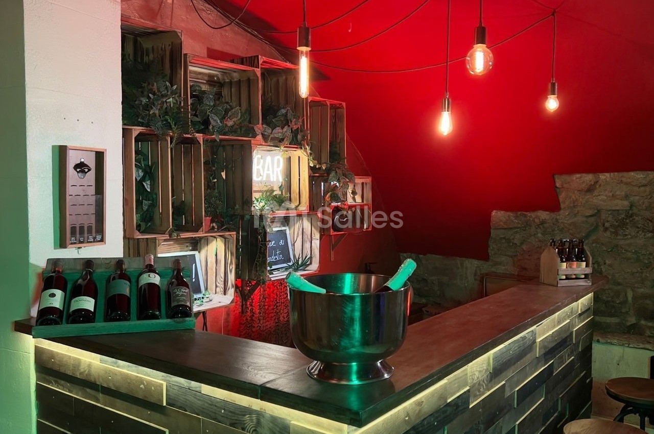 Bar en bois avec bouteilles de vin exposées, seau à glace sur le comptoir et éclairage suspendu dans une ambiance…