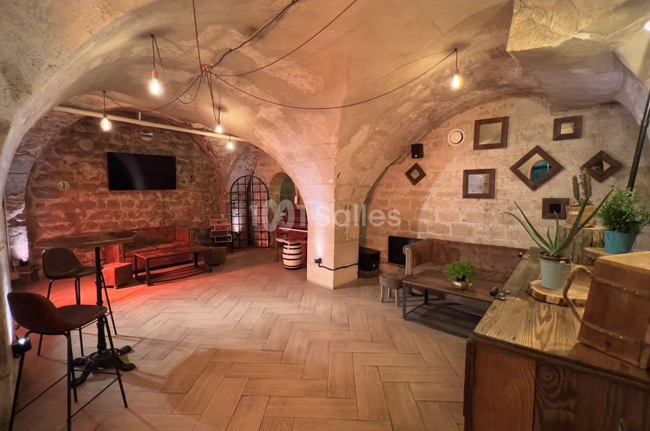 Salle voûtée en pierres apparentes avec mobilier en bois, éclairage tamisé et décorations murales.