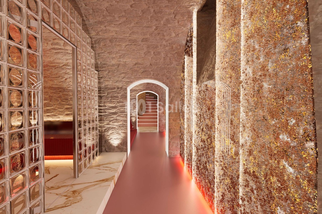 Couloir voûté avec murs texturés dorés, sol lisse et éclairage tamisé menant à un escalier en pierre.