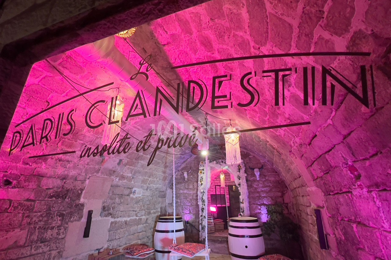 Salle voûtée en pierre éclairée de lumières roses, avec des tonneaux et une inscription ’Paris Clandestin’.