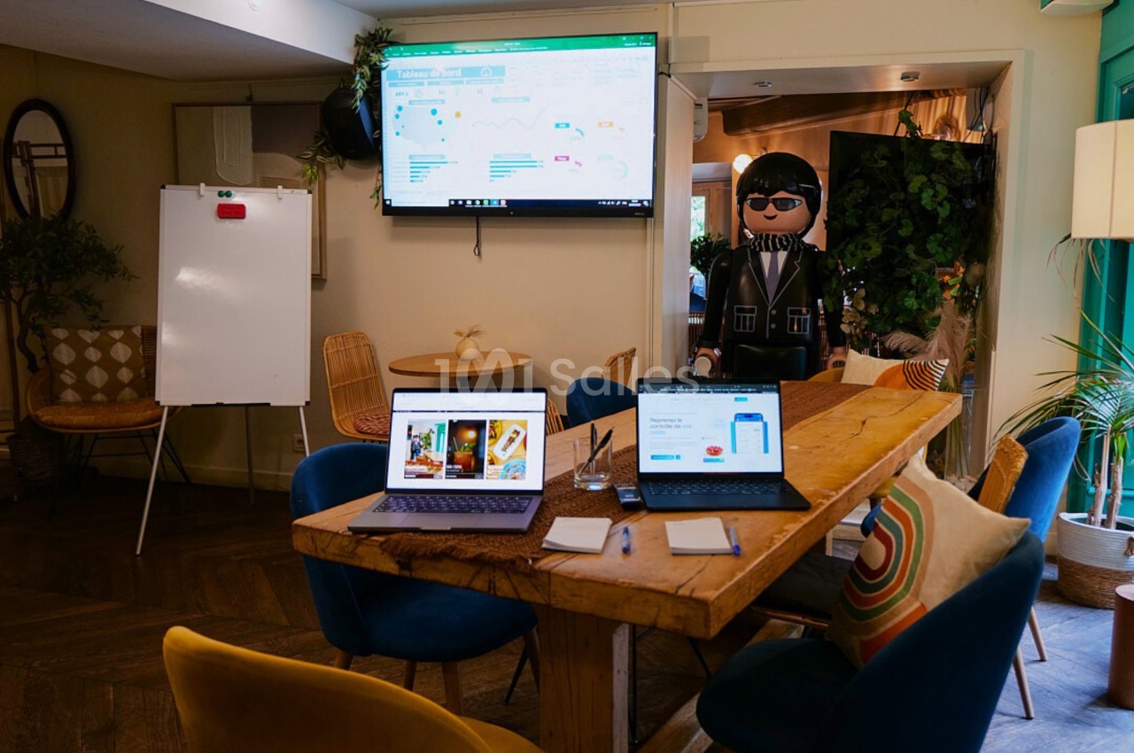 Salle de réunion avec deux ordinateurs portables sur une table en bois, un tableau blanc et un écran affichant des données.