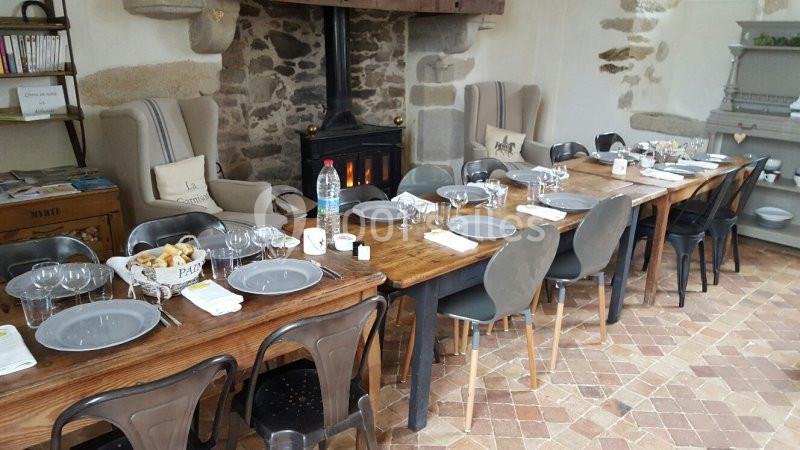 Table en bois dressée pour un repas, entourée de chaises, dans une pièce avec cheminée et murs en pierre.