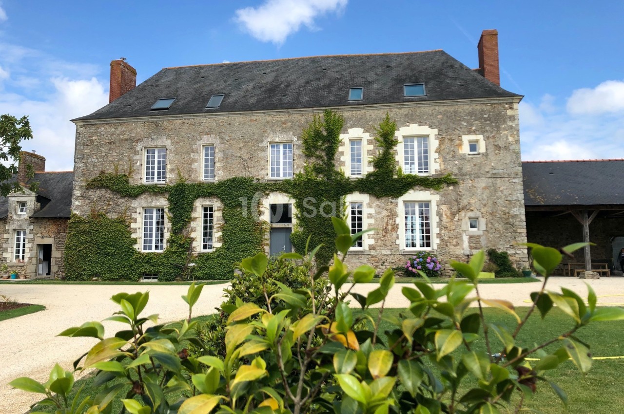Façade d'une maison en pierre avec des volets blancs, des plantes grimpantes et un jardin au premier plan.
