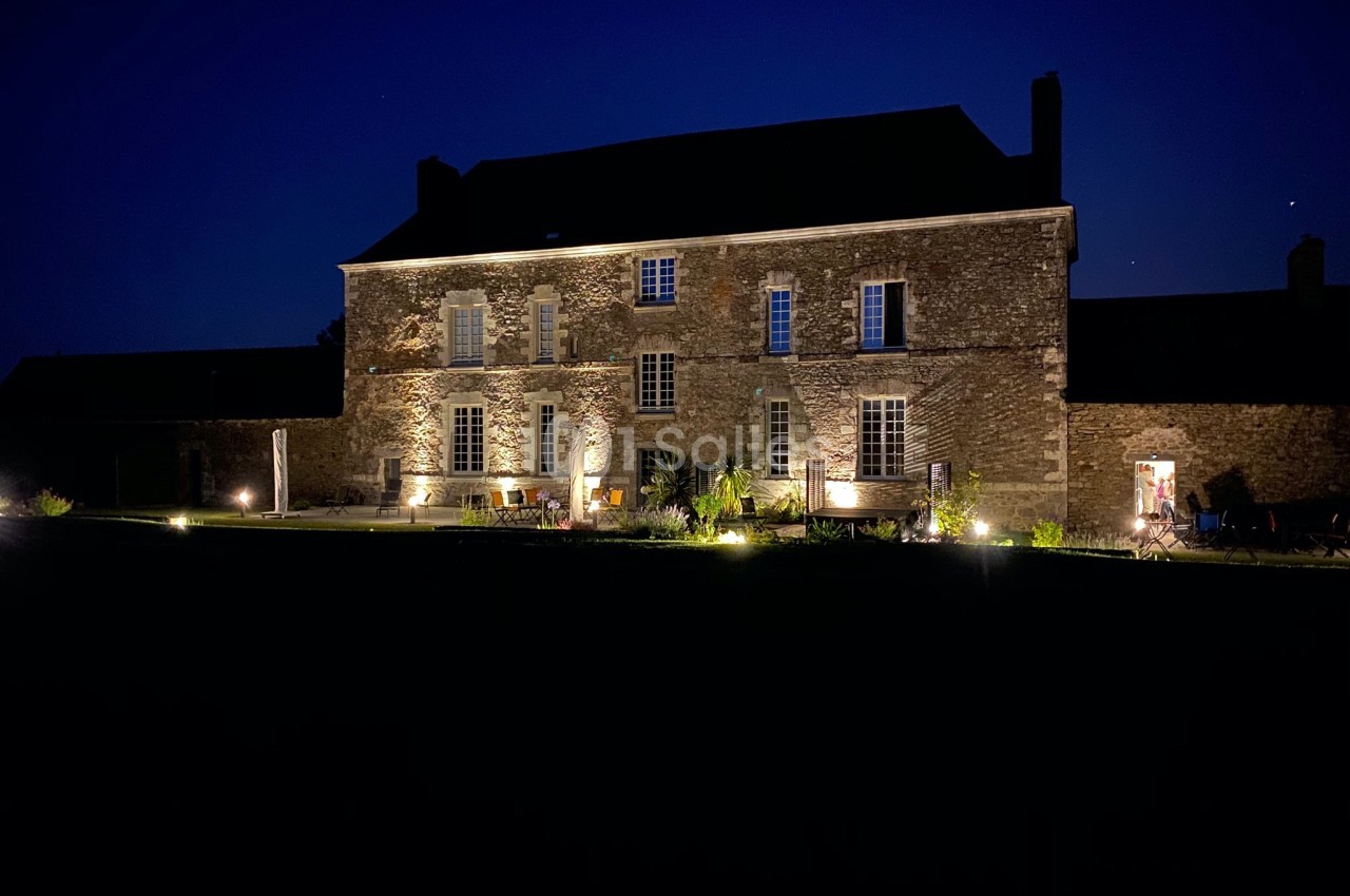 Façade d'une grande maison en pierre éclairée par des lumières extérieures, photographiée de nuit.