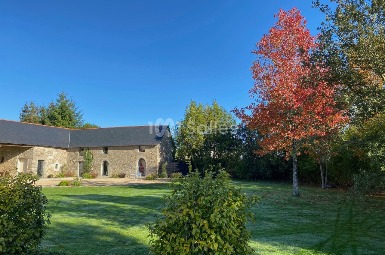 Cour verdoyante avec pelouse, arbres aux feuilles rouges et bâtiment en pierre sous un ciel bleu clair.