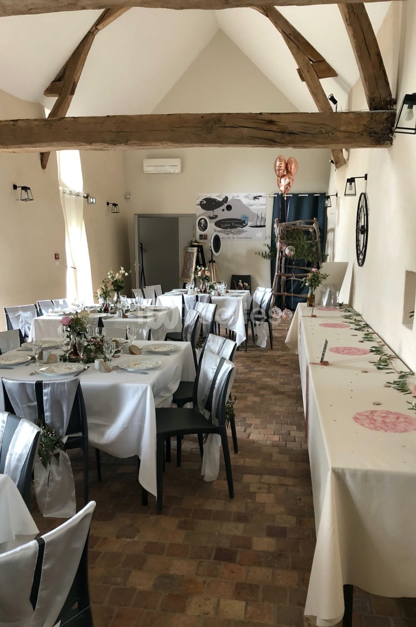 Salle de réception décorée avec des tables dressées, nappes blanches, fleurs et ballons en forme de cœur.