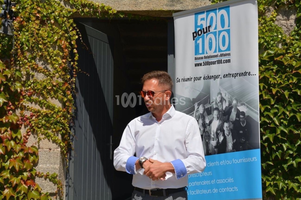 Un homme en chemise blanche parle devant une porte ouverte, à côté d'une bannière d'un réseau professionnel.