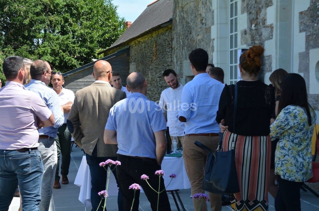 Un groupe de personnes discute à l'extérieur près d'un bâtiment en pierre, sous un ciel ensoleillé.