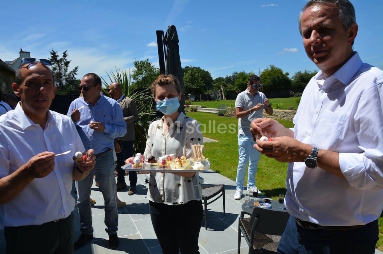 Des personnes dégustent des amuse-bouches en extérieur, sous un ciel ensoleillé, dans un jardin.