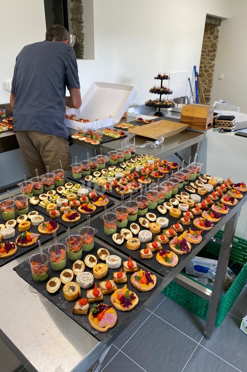 Un traiteur prépare des plateaux de bouchées apéritives variées dans une cuisine professionnelle.