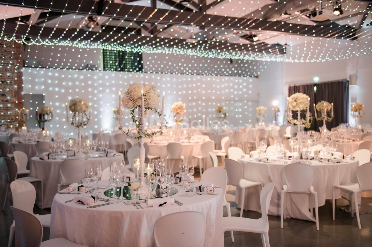 Salle de réception dressée avec tables rondes, chaises blanches et compositions florales - plafond illuminé de points lumineux.