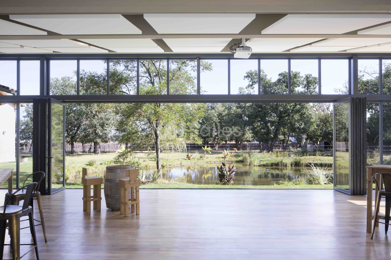 Salle intérieure avec baies vitrées surplombant un étang, arbres et parc arborisé - sol en bois.