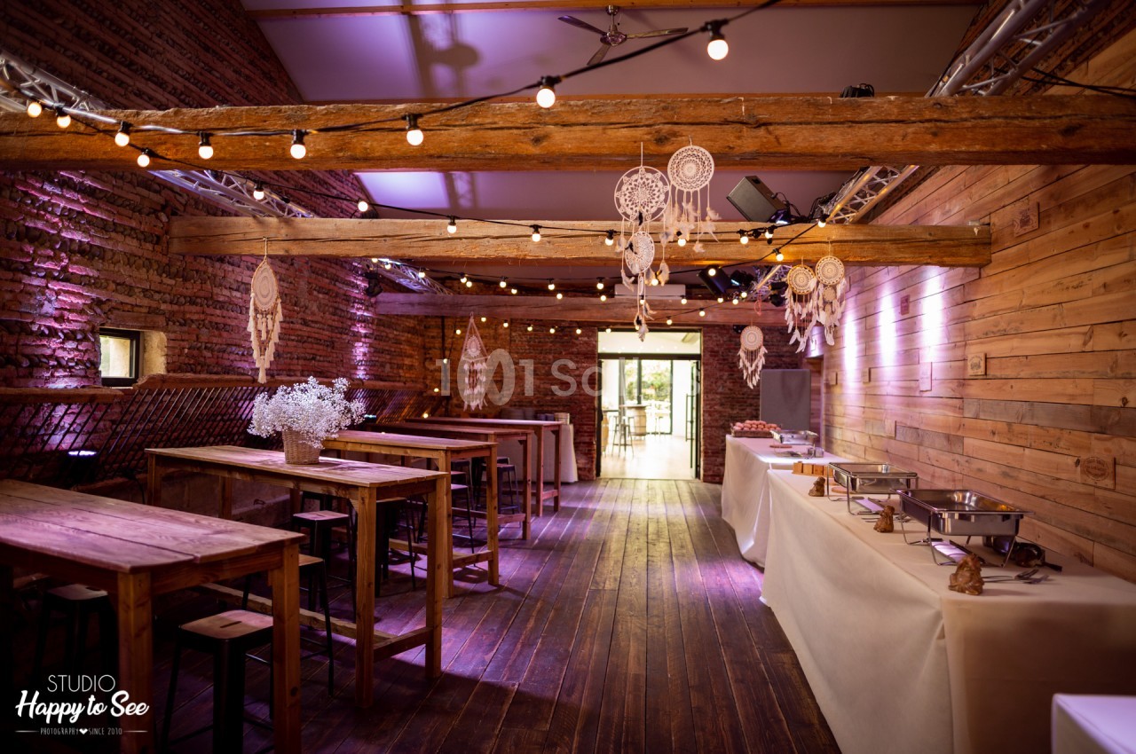 Salle intérieure avec murs en brique et bois, poutres apparentes, tables en bois, éclairage violet et guirlandes lumineuses, dreamcatchers suspendus.