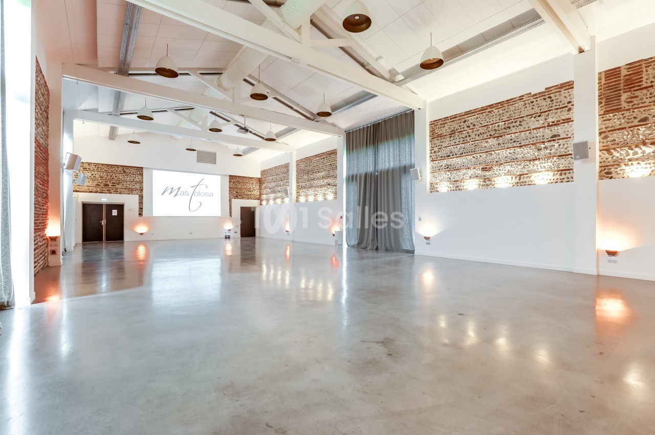 Salle vide à sol béton, murs en brique rouge, plafond blanc avec luminaires, écran et rideaux gris.