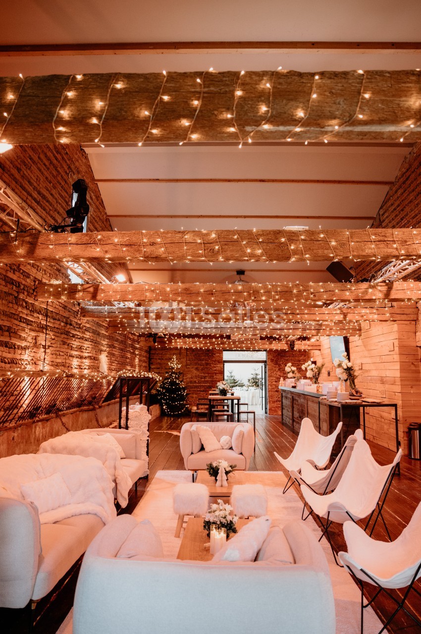 Intérieur en briques avec poutres apparentes, guirlandes lumineuses, fauteuils blancs et canapés autour de tables basses.