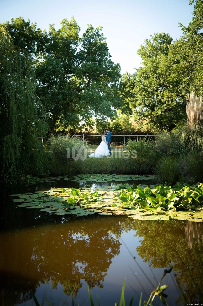 Couple en tenue de mariage près d'un étang bordé de végétation luxuriante et d'arbres.