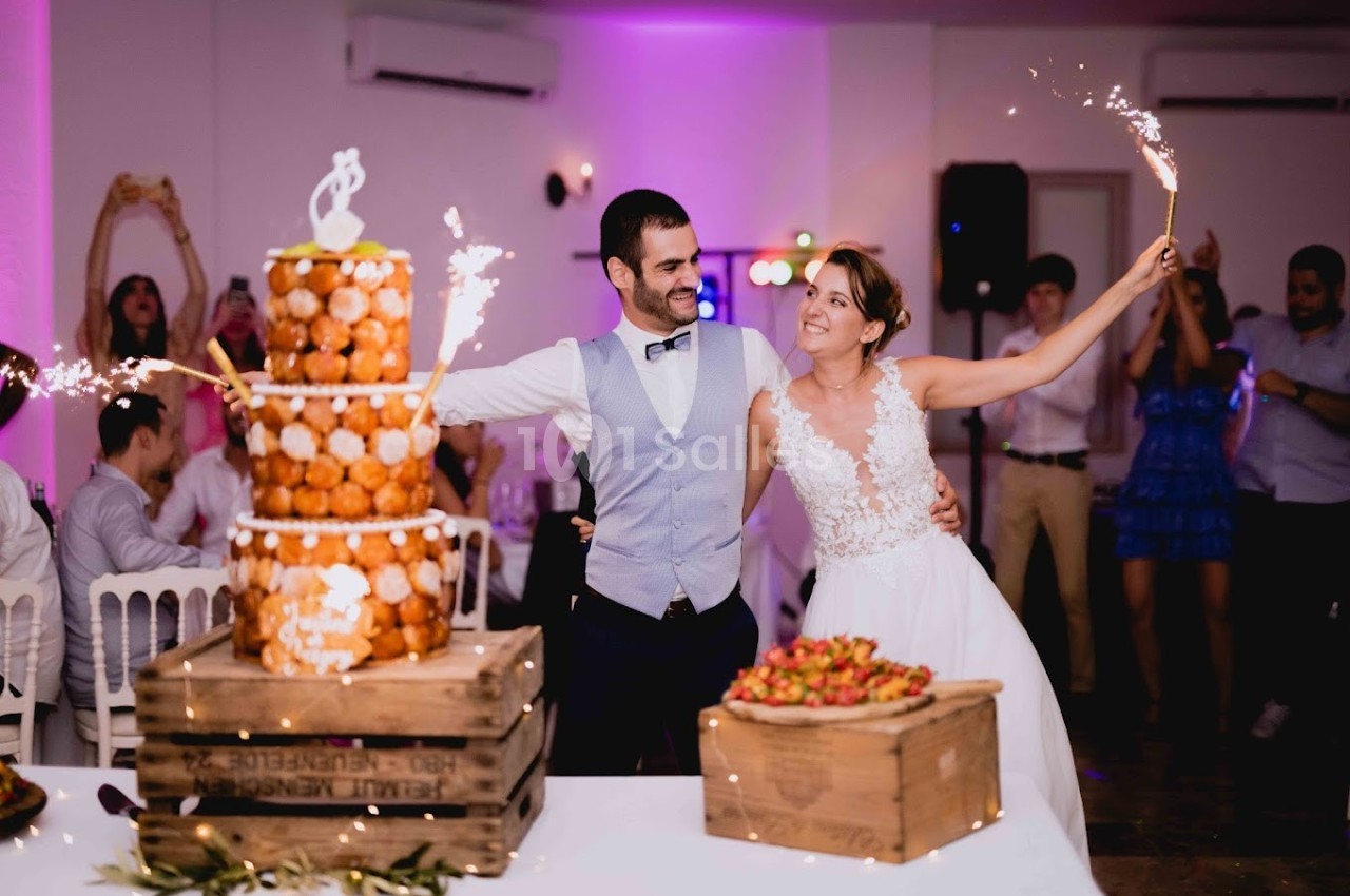 Un couple de mariés souriants tient des cierges magiques près d'une pièce montée et de fraises lors de leur réception.