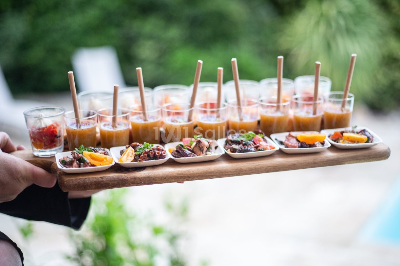 Plateau de verrines et bouchées apéritives colorées, présenté en extérieur près d'un jardin verdoyant.