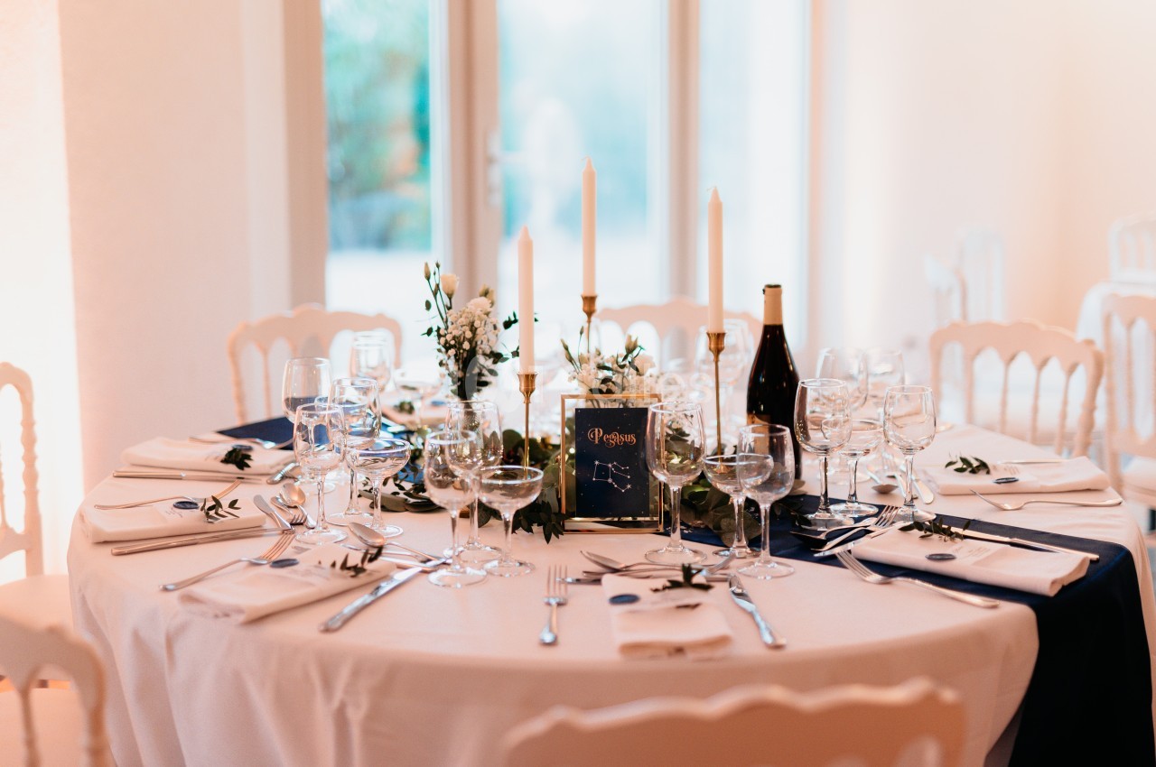 Table élégamment dressée avec nappes blanches, bougies, vaisselle raffinée et décoration florale.