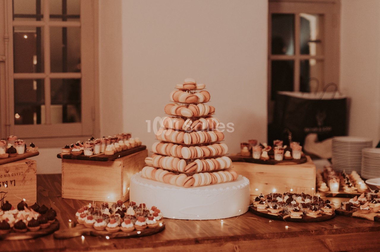 Tour de macarons sur une table en bois entourée de petits desserts variés dans une salle éclairée chaleureusement.