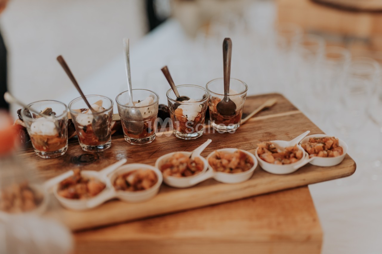 Plateau en bois avec verrines et petites coupelles contenant des préparations culinaires, accompagné de cuillères.