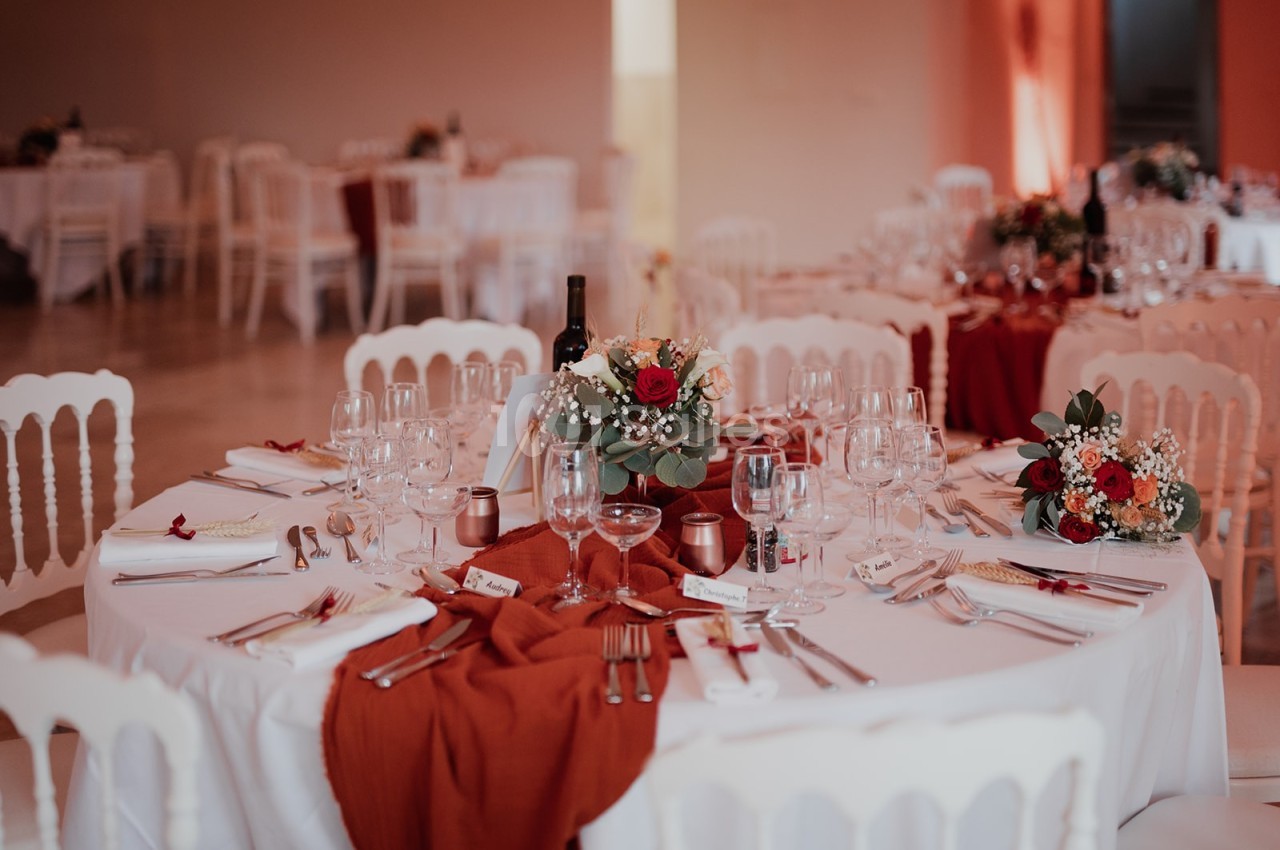 Table de réception décorée avec des nappes blanches, chemins de table rouges, fleurs et vaisselle élégante.