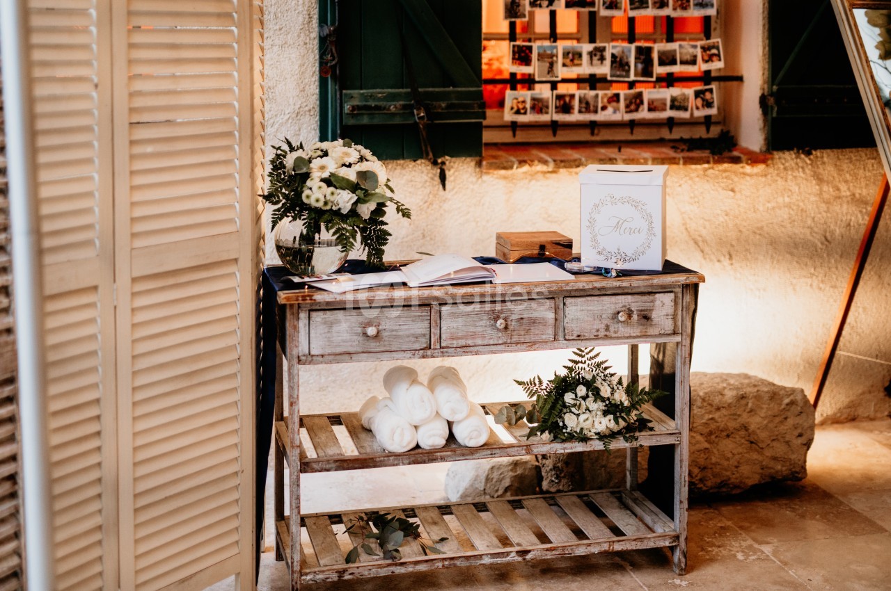 Table en bois décorée avec des fleurs blanches, des serviettes roulées et une urne, dans un cadre rustique.