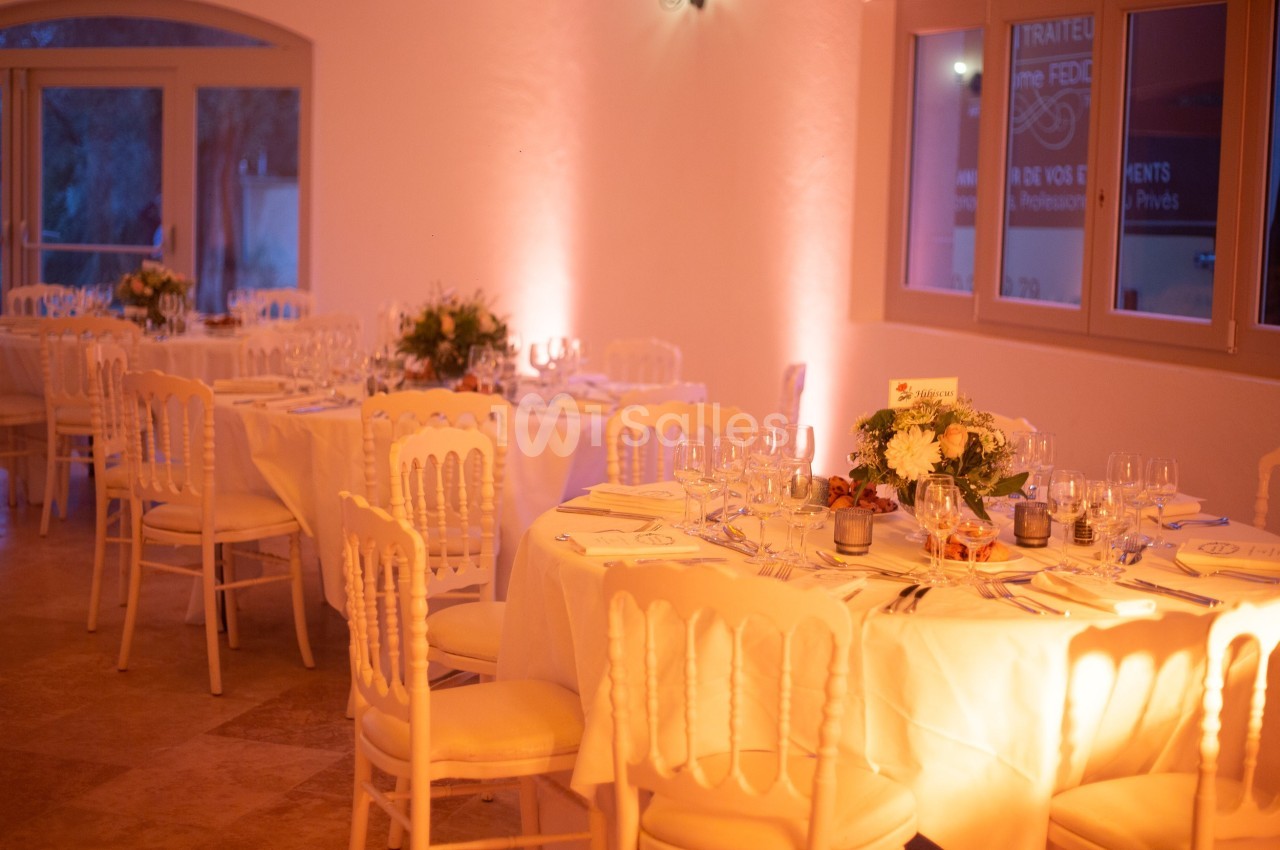 Salle de réception élégante avec tables rondes dressées, nappes blanches et décoration florale.