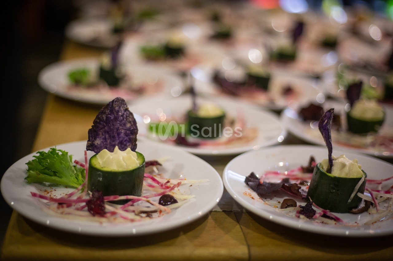 Assiette de présentation avec roulé de concombre garni de mousse, décoré de chips violettes et légumes colorés.