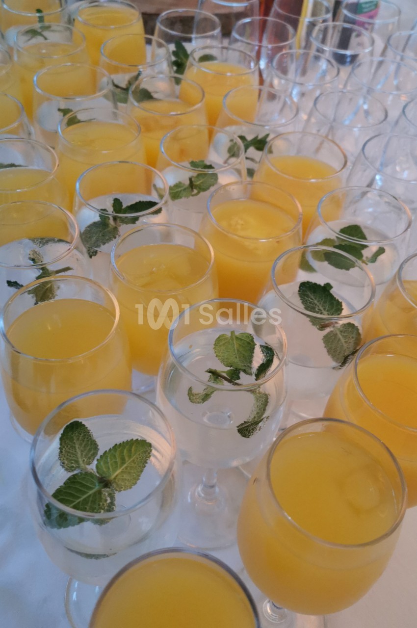 Verres de jus d'orange et d'eau garnie de feuilles de menthe disposés sur une table blanche.