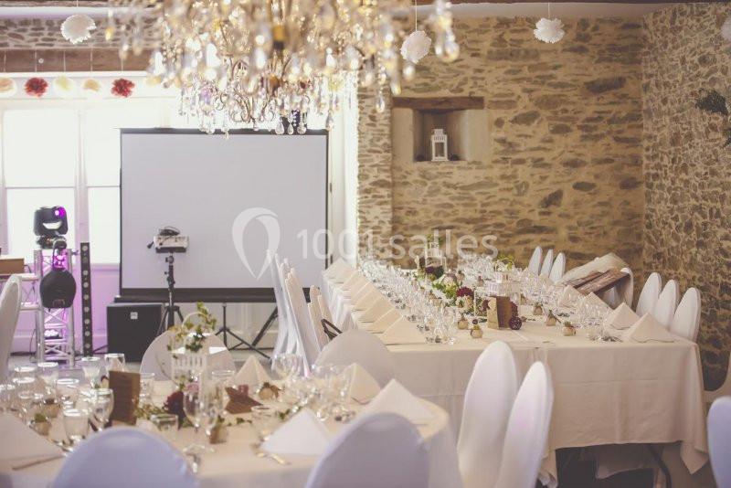 Salle de réception avec tables dressées, nappes blanches, chaises couvertes et décorations élégantes sous un lustre.