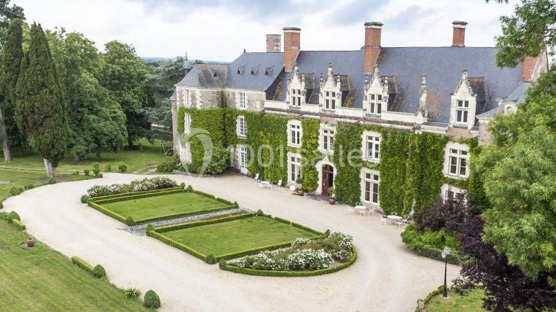 Façade d'un château recouvert de lierre, entouré de jardins soignés et d'une allée gravillonnée.