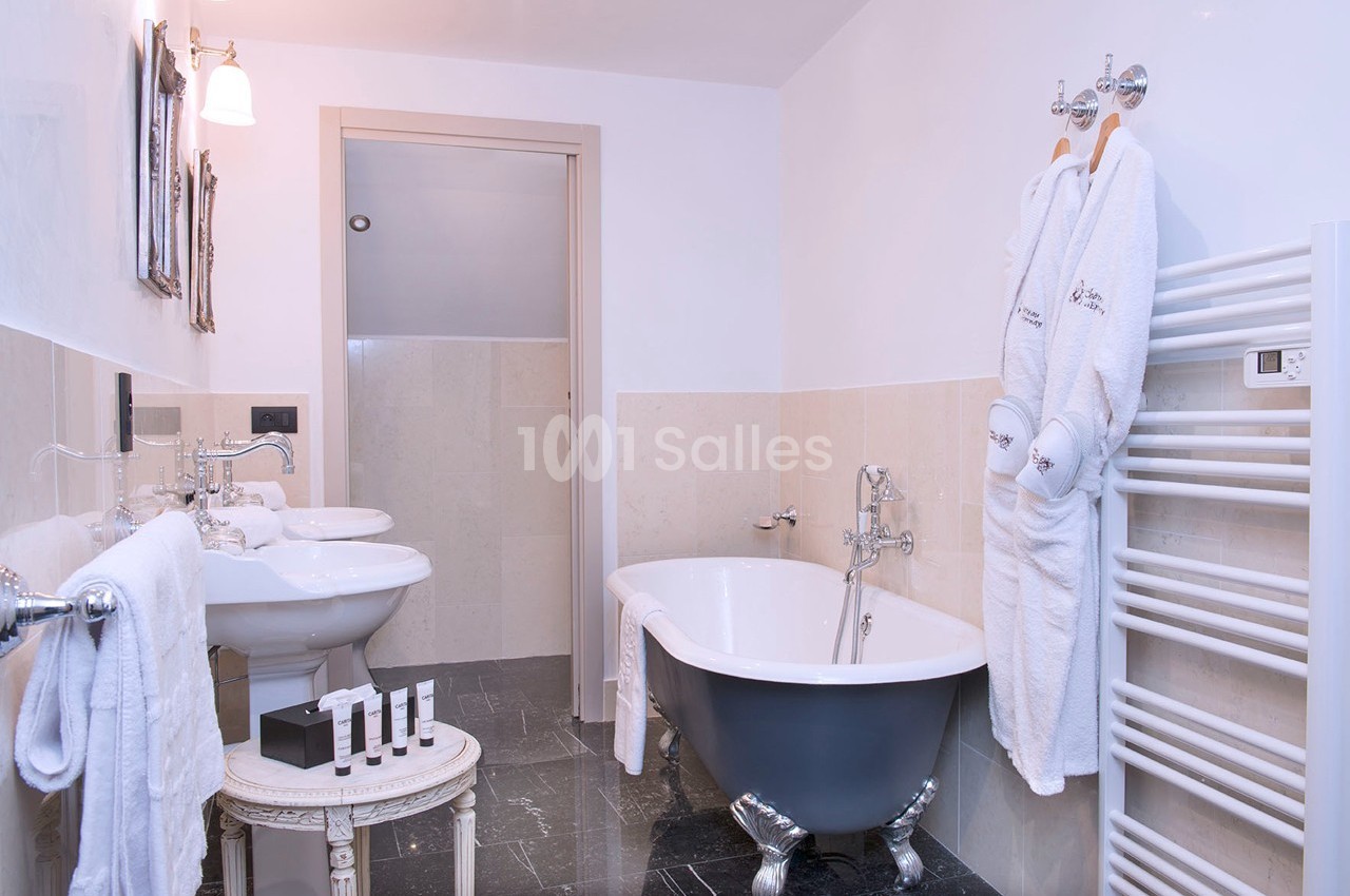 Salle de bain avec baignoire sur pieds, double vasque, radiateur sèche-serviettes et peignoirs accrochés.