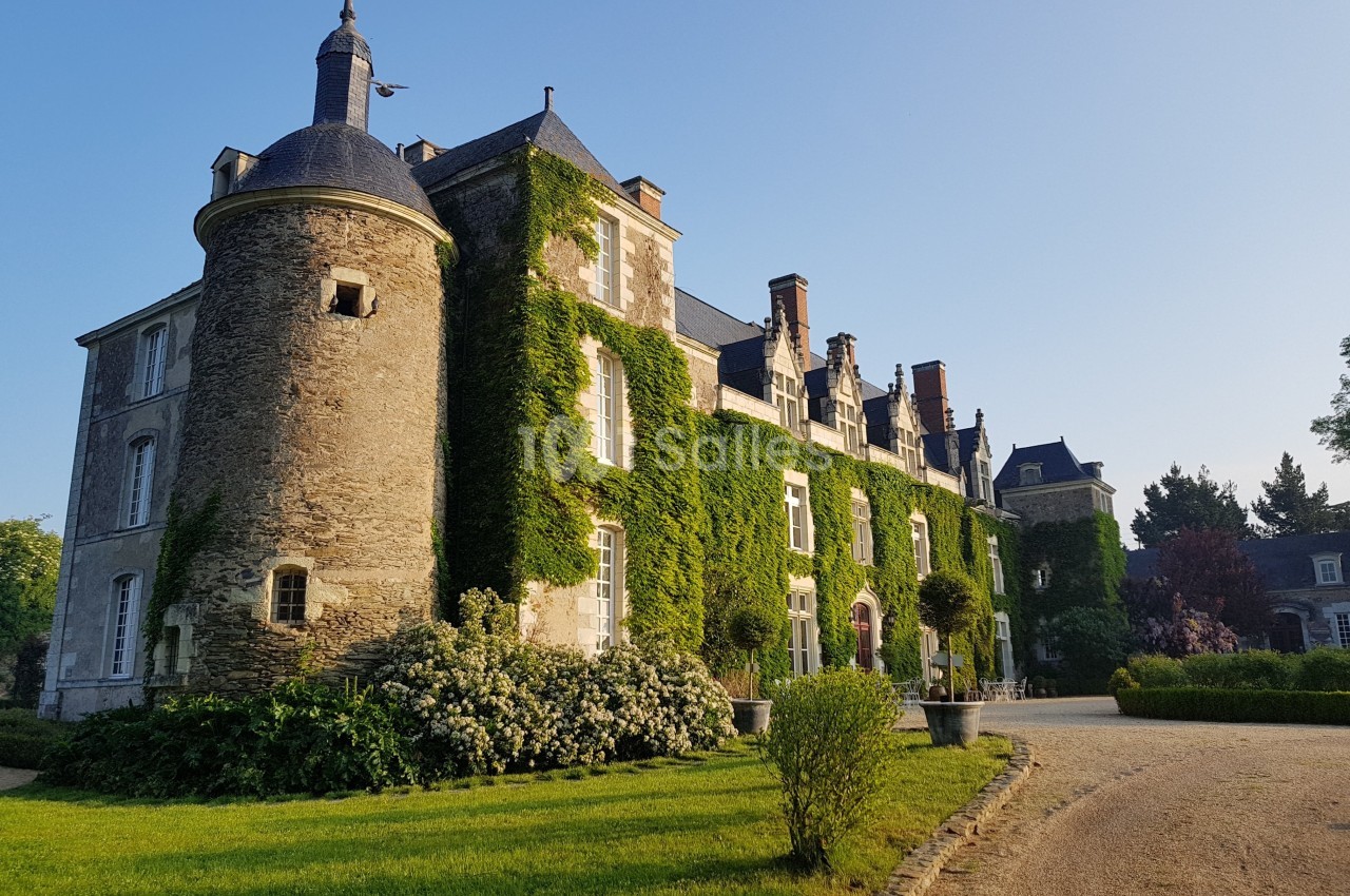 Façade d'un château en pierre recouvert de lierre, entouré de jardins et baigné par une lumière douce.